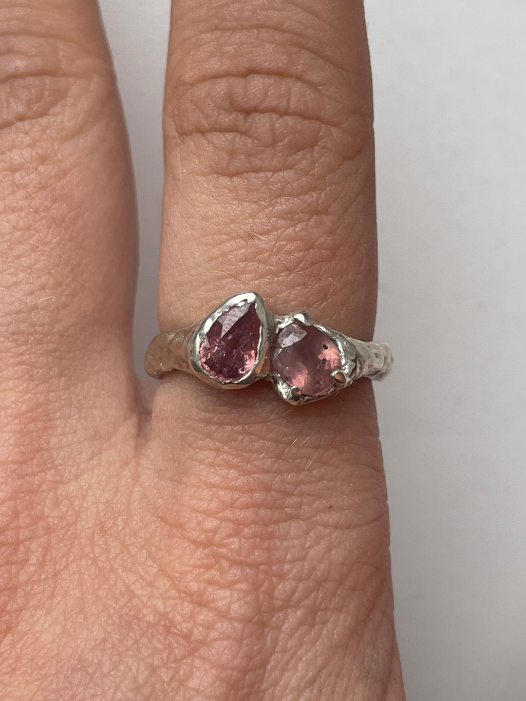 Bespoke silver ring with two pink sapphires on a person's finger.