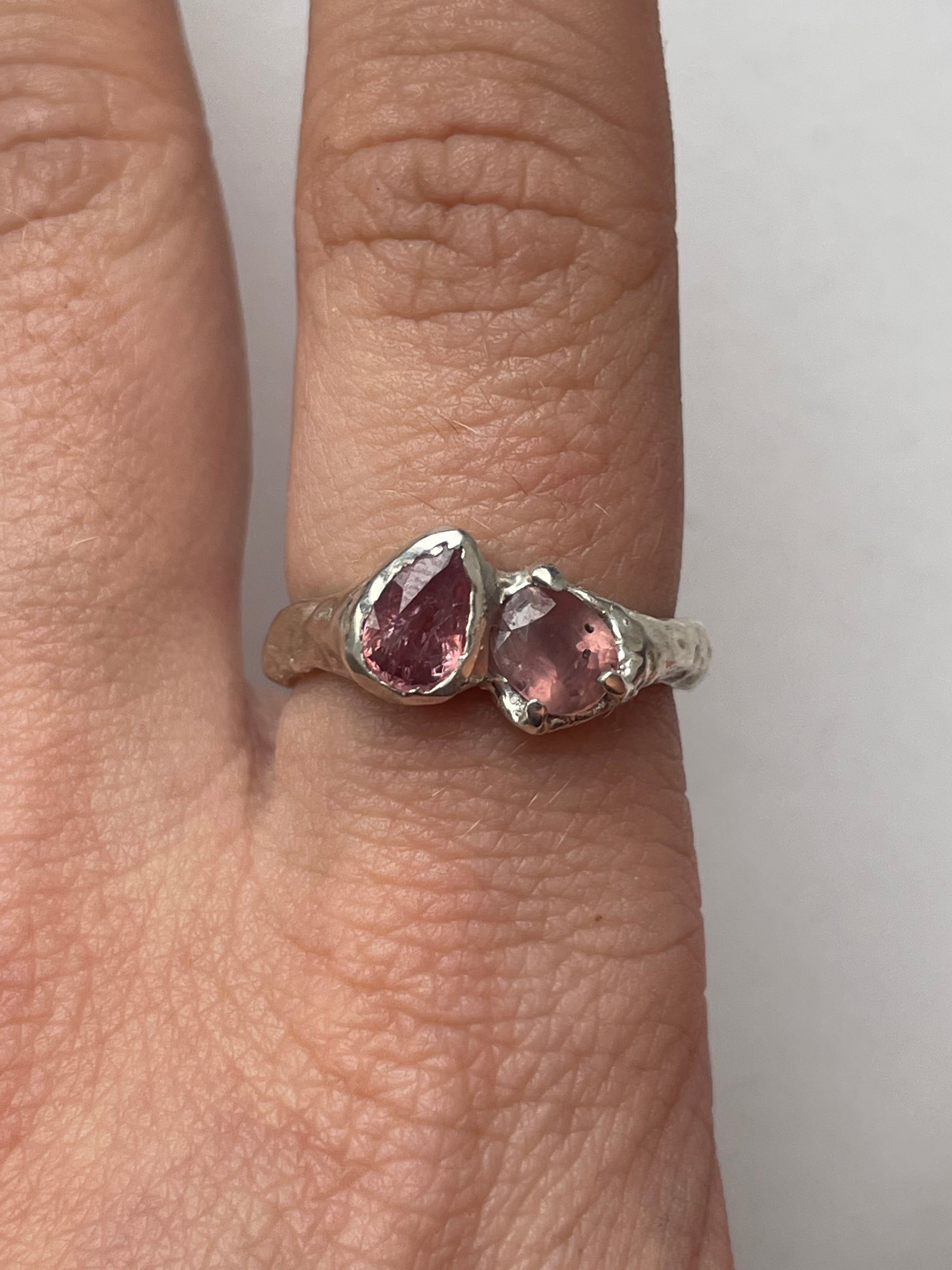 Bespoke silver ring with two pink sapphires on a person's finger.